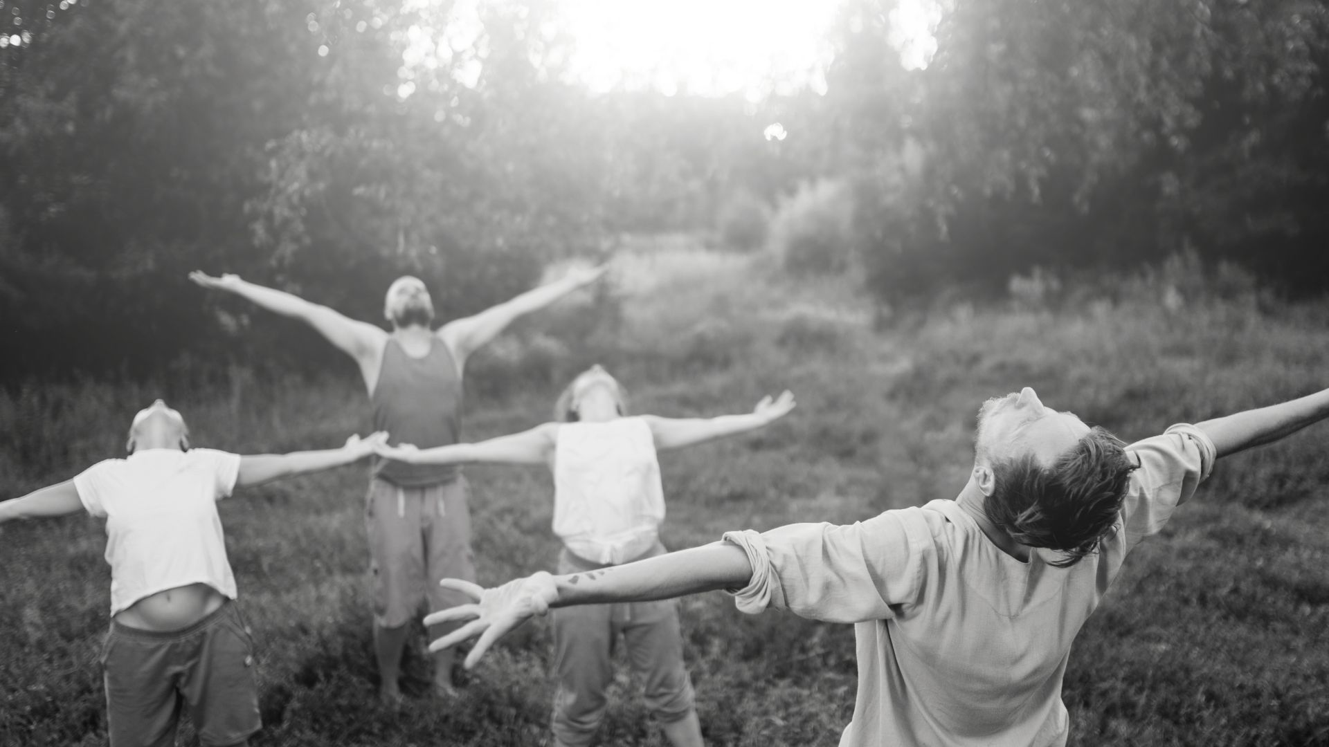 Una foto in bianco e nero di un gruppo di persone all'aperto con le braccia spalancate, che sembrano abbracciare la natura. Il sole filtra attraverso gli alberi, aggiungendo una luce serena alla scena, catturando l'essenza di un'esperienza di digital detox mentre si connettono con l'ambiente naturale.